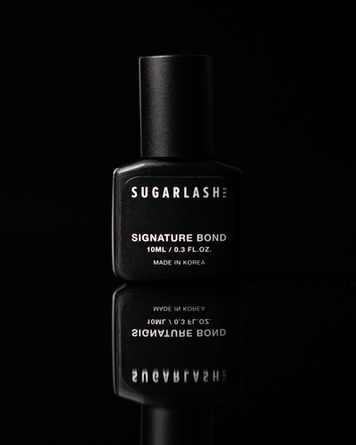 A bottle of lash extension glue with it's reflection showing underneath the bottle.