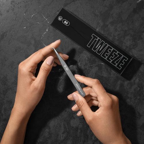 Model holding a lash extensions Universal Tweezer U-90 near its box.
