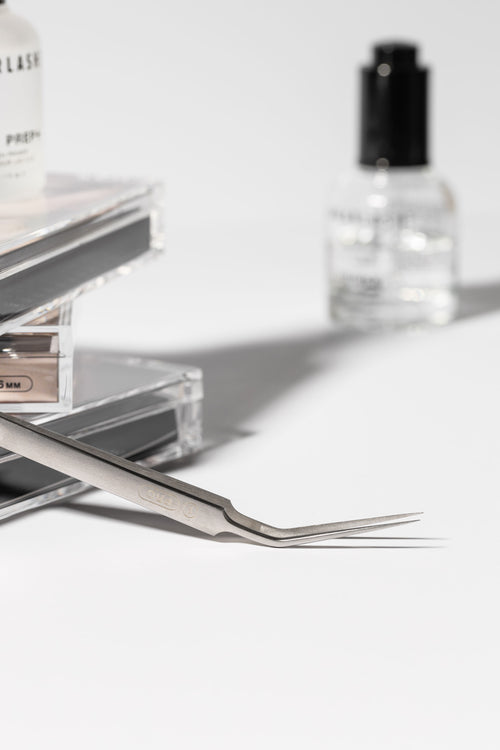 An I-PRO tweezer with an array of products in the background, eyelash extensions