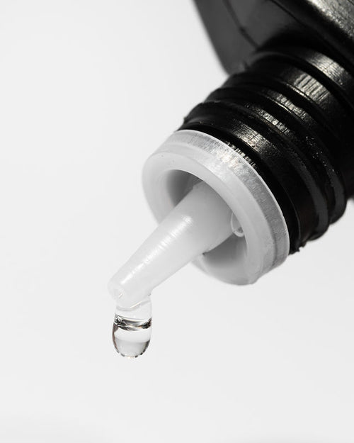 A drop coming out of a bottle of Naked Bond eyelash extension adhesive.