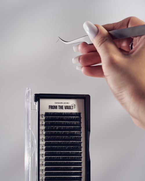 A model holding tweezers over an open tray of Flat Lashes.
