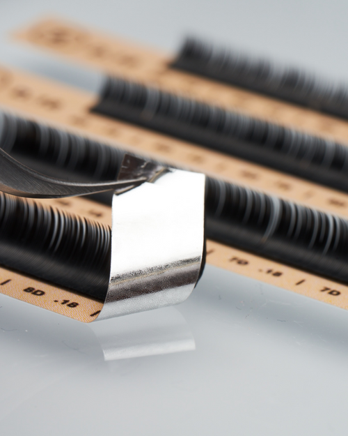 Tweezers peeling up a strip of Flat eyelash extensions.
