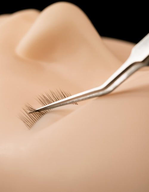 Close up of tweezers being used on Mannequin Head with Lashes.