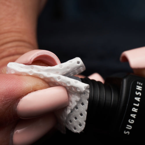 Adhesive wipe being used to clean the nozzle of a bottle of lash extension adhesive 