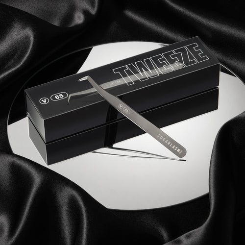 A box of lash extension Volume Tweezer V-65 on top of a mirror with an unboxed pair of tweezers resting partially on the box.
